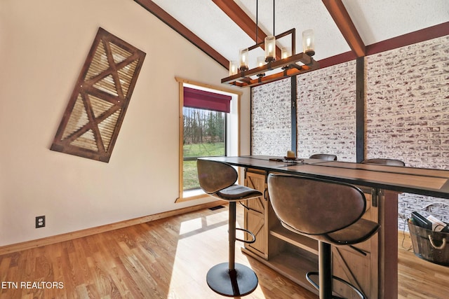 dining area featuring a notable chandelier, lofted ceiling with beams, and light wood-type flooring