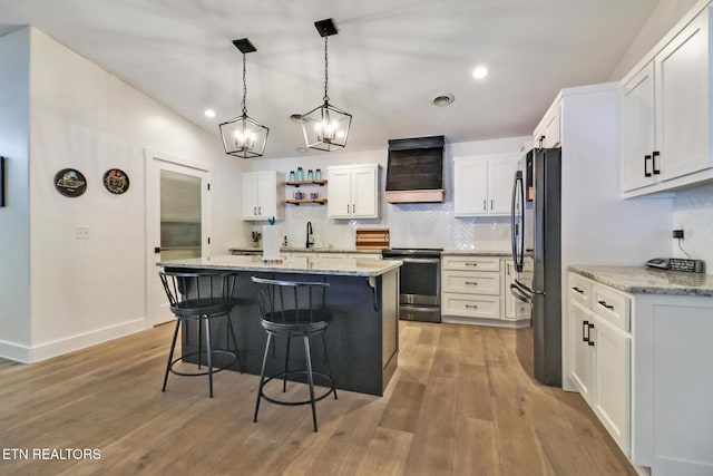 kitchen with an island with sink, white cabinets, electric range, black fridge, and light hardwood / wood-style flooring