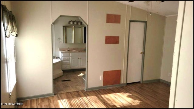 unfurnished bedroom with light wood-type flooring, connected bathroom, sink, and multiple windows