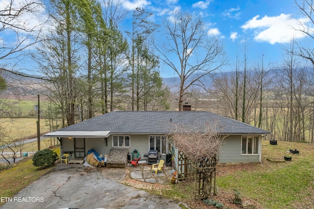 rear view of house with entry steps, driveway, a shingled roof, and a chimney