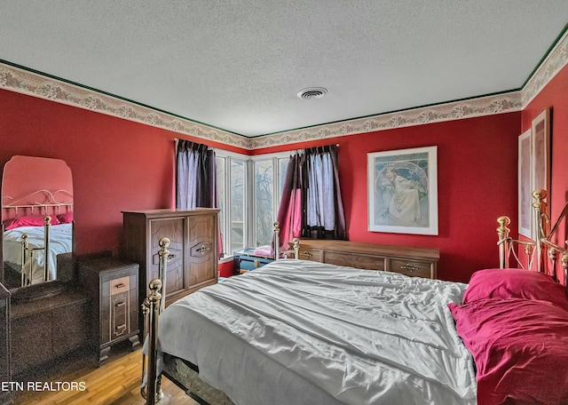 bedroom with a textured ceiling, wood finished floors, and visible vents