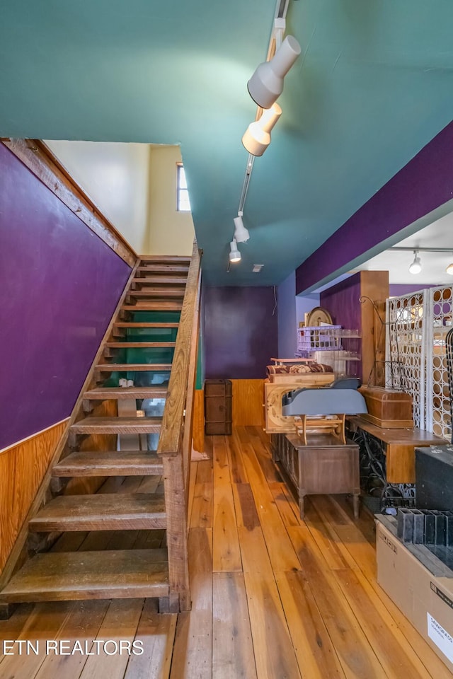 staircase featuring a wainscoted wall, wood walls, rail lighting, and hardwood / wood-style flooring