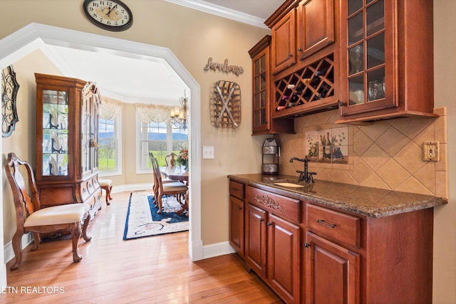 bar with sink, light hardwood / wood-style flooring, ornamental molding, dark stone counters, and backsplash