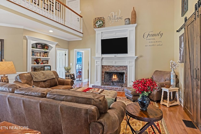 living room with a brick fireplace, ornamental molding, a towering ceiling, a barn door, and light hardwood / wood-style floors