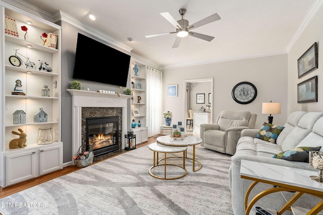 living room with a fireplace, built in features, ornamental molding, light wood-type flooring, and ceiling fan