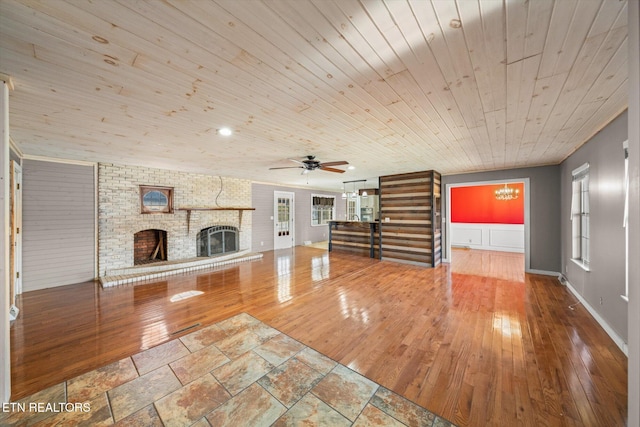 unfurnished living room with brick wall, ceiling fan with notable chandelier, a fireplace, hardwood / wood-style flooring, and wooden ceiling