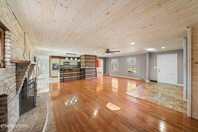 unfurnished living room featuring a brick fireplace, wooden ceiling, ceiling fan, and light wood-type flooring