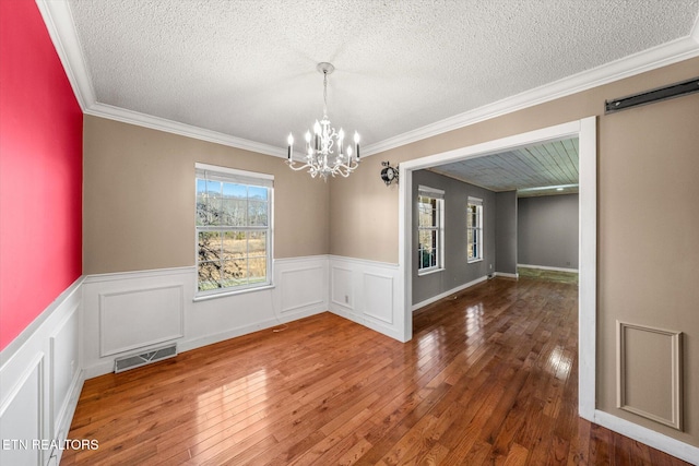 unfurnished dining area with an inviting chandelier, ornamental molding, hardwood / wood-style floors, and a textured ceiling