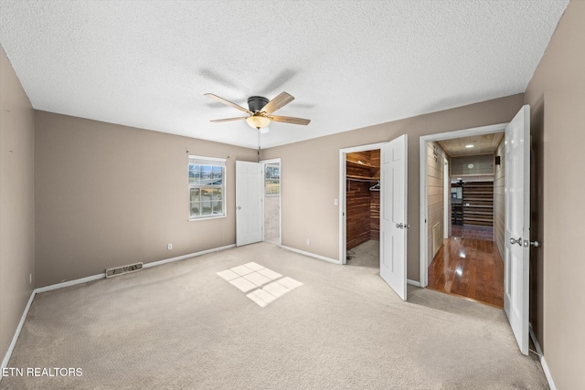 unfurnished bedroom featuring a walk in closet, light carpet, a textured ceiling, a closet, and ceiling fan