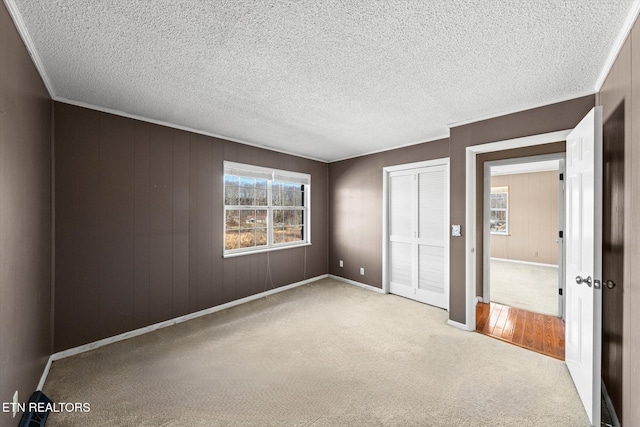 unfurnished bedroom with crown molding, light carpet, wooden walls, and a closet