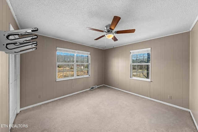 unfurnished room featuring crown molding, wooden walls, light colored carpet, and ceiling fan