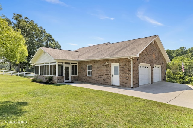 back of property featuring a lawn, a garage, and a sunroom