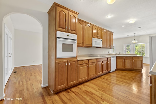 kitchen with kitchen peninsula, decorative light fixtures, sink, white appliances, and light hardwood / wood-style floors