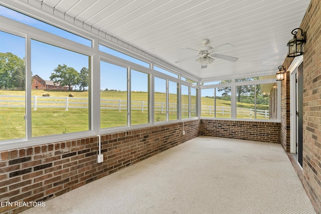 unfurnished sunroom featuring ceiling fan and a rural view