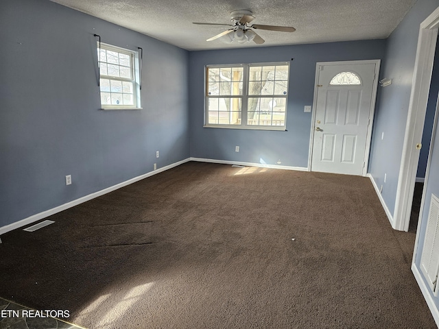 foyer entrance with ceiling fan, a textured ceiling, and dark colored carpet