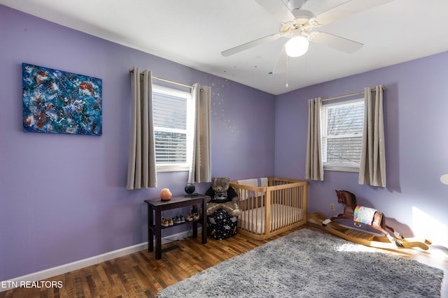 bedroom featuring a nursery area, dark hardwood / wood-style floors, and ceiling fan