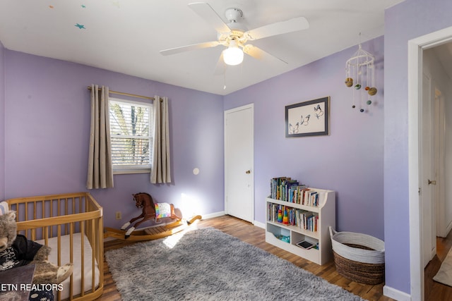 bedroom with a nursery area, ceiling fan, and hardwood / wood-style flooring