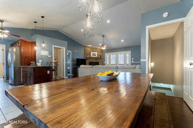 dining space featuring ceiling fan, a stone fireplace, and vaulted ceiling