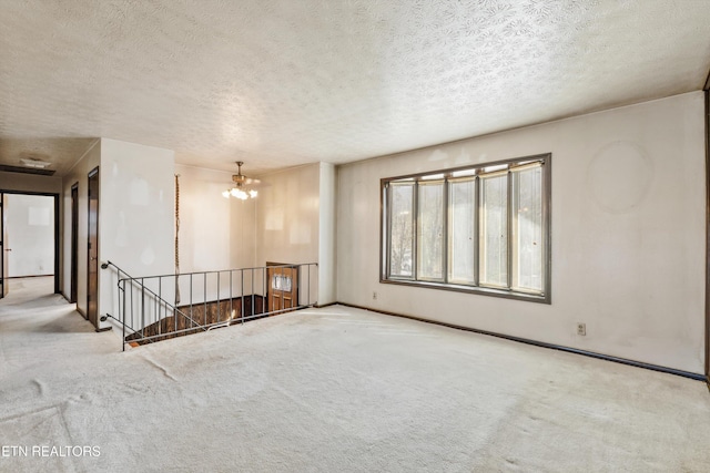 empty room with light carpet, a textured ceiling, and a notable chandelier