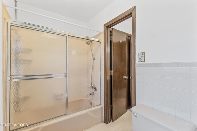 bathroom featuring tile walls, toilet, and combined bath / shower with glass door