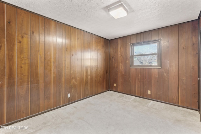 carpeted spare room featuring wooden walls and a textured ceiling