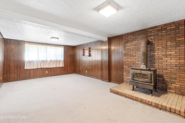 unfurnished living room featuring wood walls, a textured ceiling, a wood stove, beamed ceiling, and light colored carpet