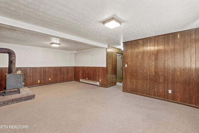 basement featuring baseboard heating, light carpet, a textured ceiling, and a wood stove