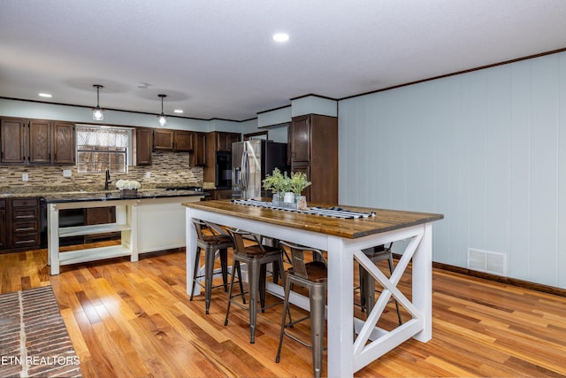 kitchen featuring stainless steel refrigerator with ice dispenser, dark brown cabinetry, tasteful backsplash, light wood-type flooring, and pendant lighting