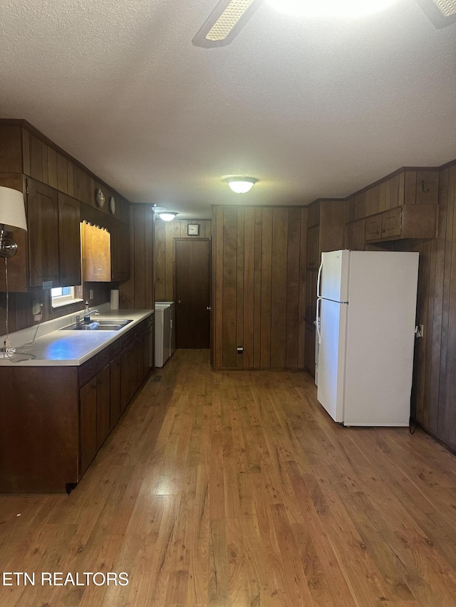 kitchen with wood walls, sink, white refrigerator, a textured ceiling, and light hardwood / wood-style flooring