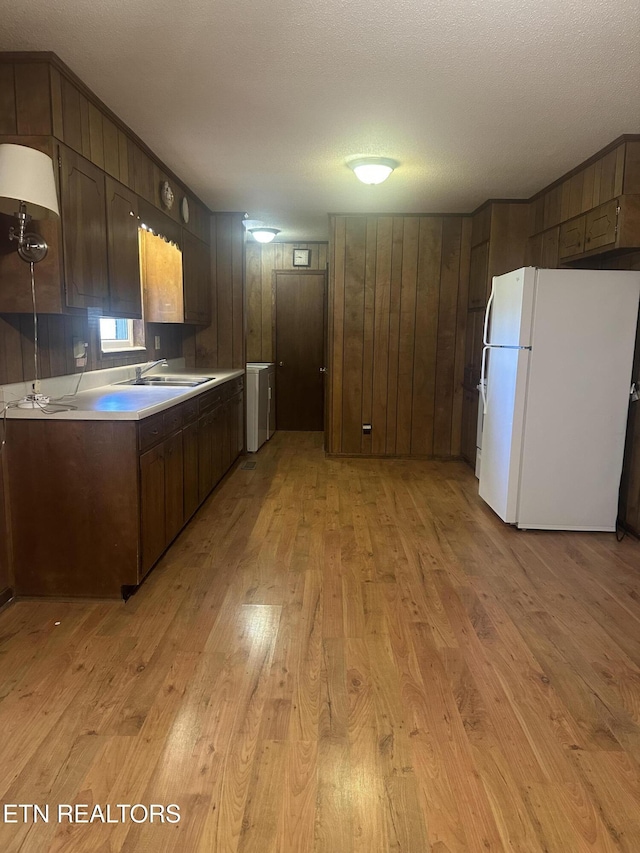 kitchen with sink, a textured ceiling, white fridge, and light wood-type flooring