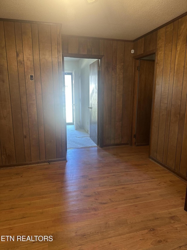 spare room featuring wooden walls, light hardwood / wood-style floors, and a textured ceiling