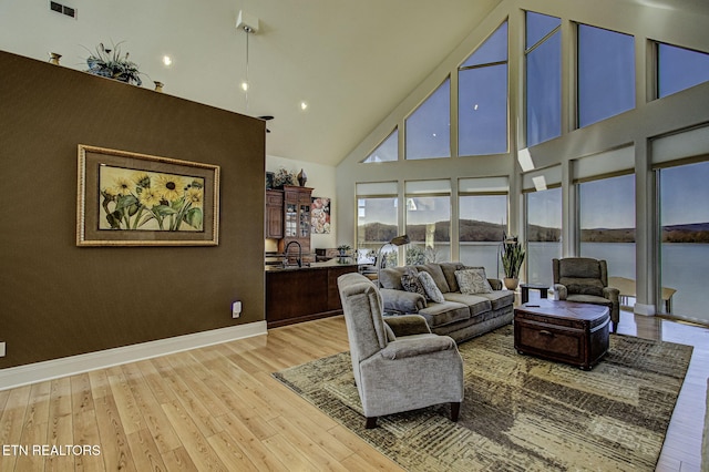 living area featuring light wood-type flooring, a water view, high vaulted ceiling, and baseboards