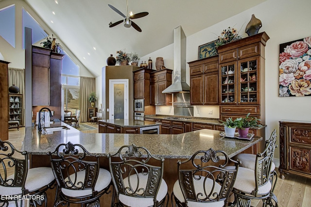 kitchen with appliances with stainless steel finishes, a sink, wall chimney range hood, light wood-type flooring, and a kitchen breakfast bar