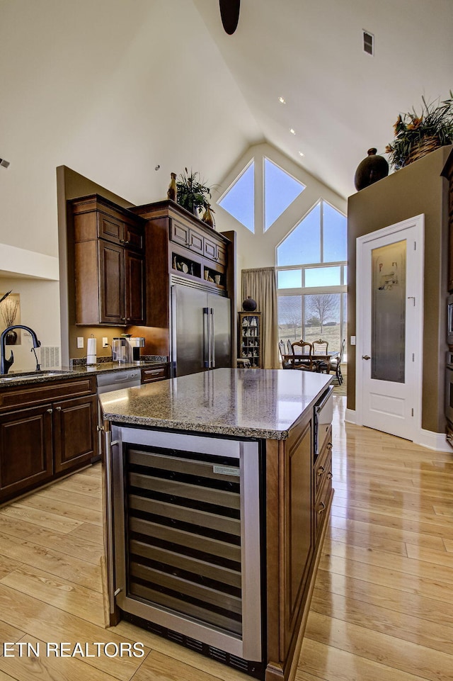 kitchen with light wood finished floors, wine cooler, stainless steel appliances, high vaulted ceiling, and a sink