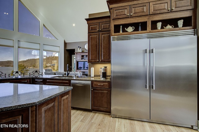 kitchen featuring light wood finished floors, open shelves, stainless steel appliances, a sink, and dark stone counters