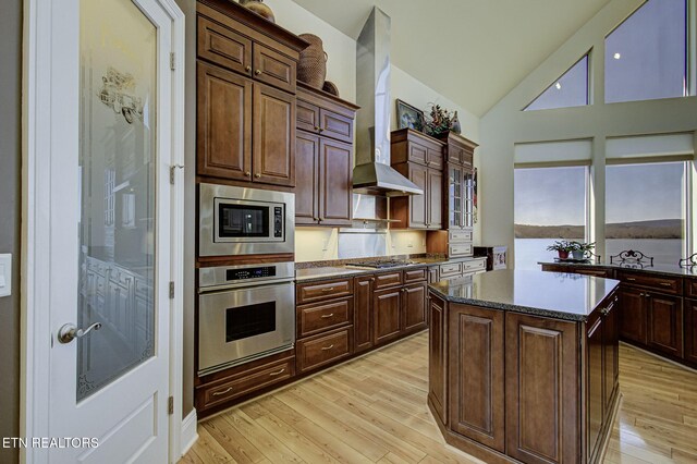 kitchen with stainless steel appliances, light wood-type flooring, a center island, and wall chimney exhaust hood