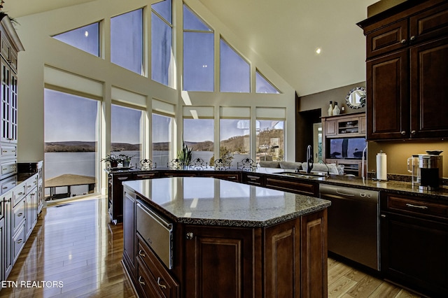 kitchen featuring dishwasher, a kitchen island, dark stone countertops, light wood-type flooring, and a sink