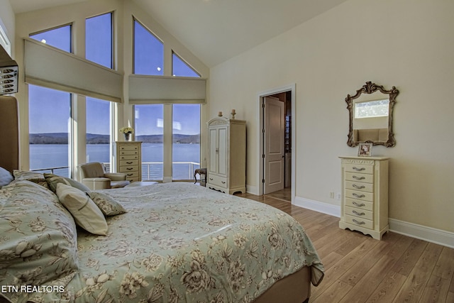 bedroom featuring high vaulted ceiling, a water view, wood finished floors, and baseboards