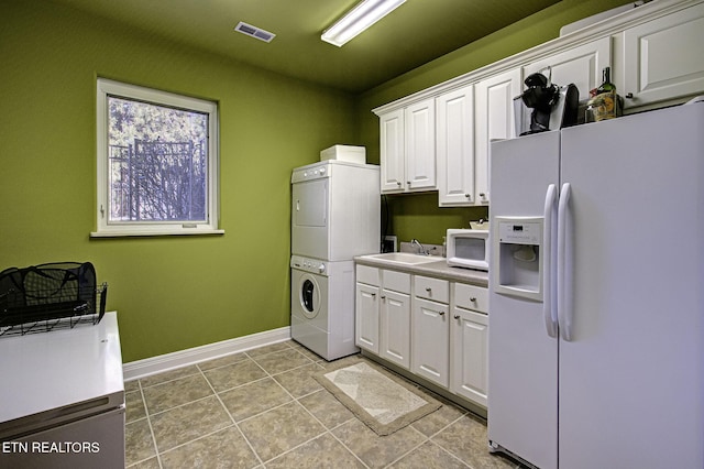 washroom featuring light tile patterned flooring, a sink, visible vents, baseboards, and stacked washer / drying machine