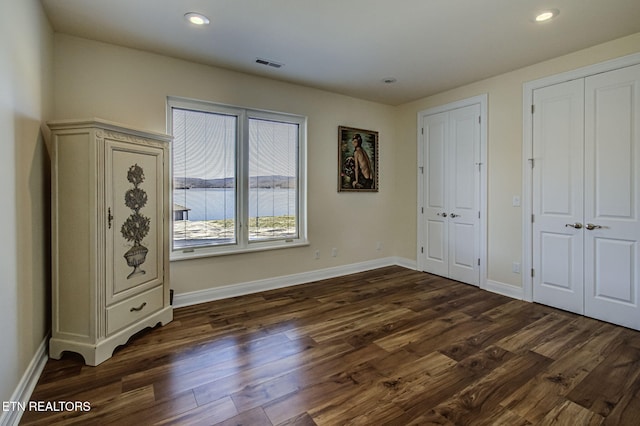 unfurnished bedroom with baseboards, visible vents, dark wood-style flooring, and two closets