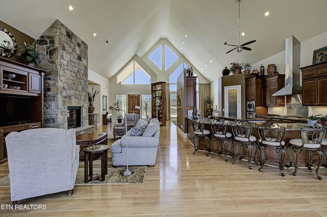 living area featuring light wood-type flooring, high vaulted ceiling, and a stone fireplace