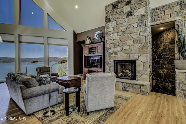 living room featuring wood-type flooring, high vaulted ceiling, and a stone fireplace