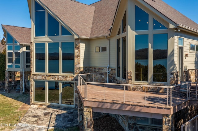 back of property featuring stone siding, roof with shingles, and a water view