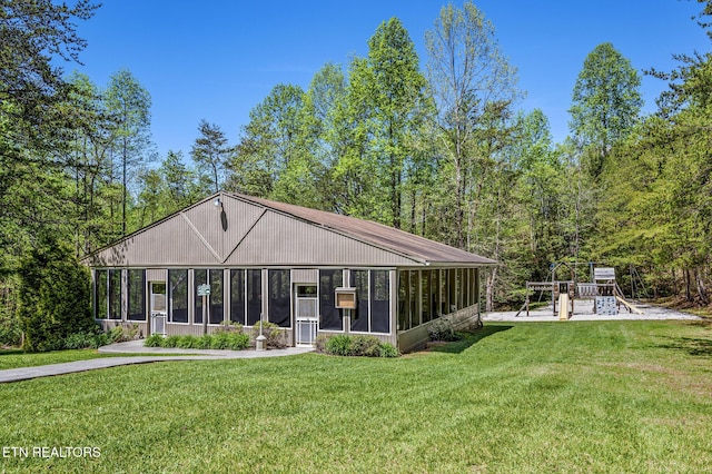 rear view of property featuring a playground, a sunroom, and a lawn