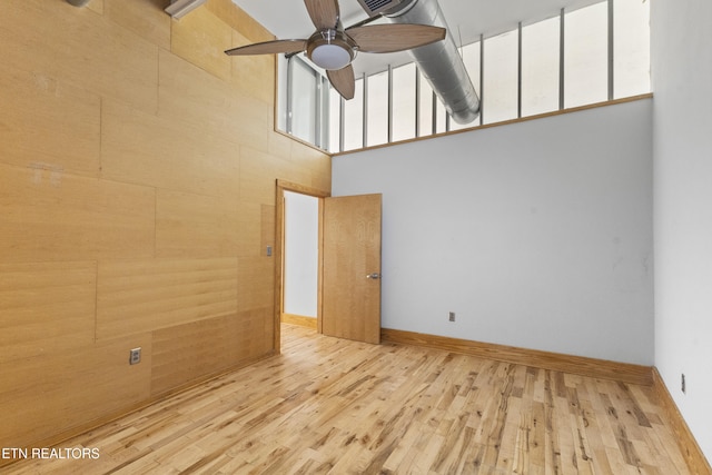 unfurnished room featuring a high ceiling, ceiling fan, and light hardwood / wood-style floors