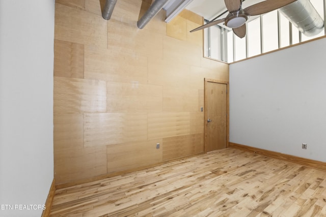 unfurnished room featuring a towering ceiling, light hardwood / wood-style flooring, and ceiling fan