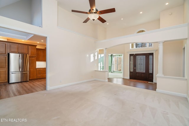 carpeted foyer entrance with ceiling fan, high vaulted ceiling, and decorative columns