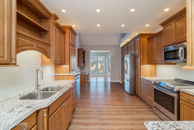 kitchen with stainless steel appliances, light stone countertops, sink, and light hardwood / wood-style flooring