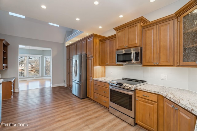 kitchen featuring stainless steel appliances, light stone counters, backsplash, and light wood-type flooring