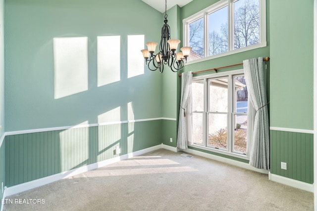 unfurnished room featuring a high ceiling, a healthy amount of sunlight, carpet floors, and an inviting chandelier